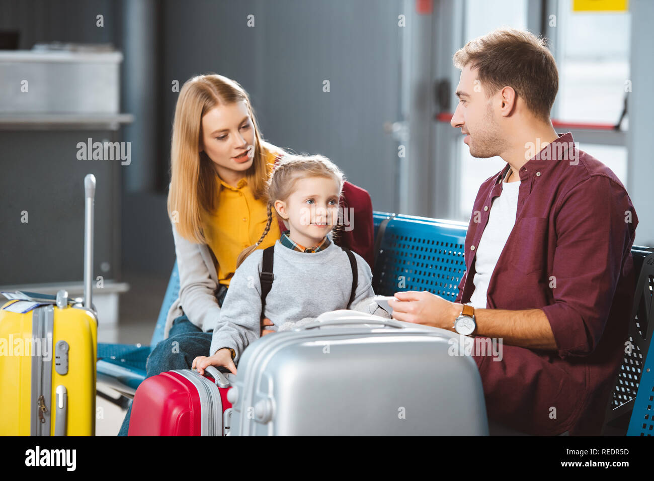 attractive mother talking with daughter near suitcases and husband in departure lounge Stock Photo