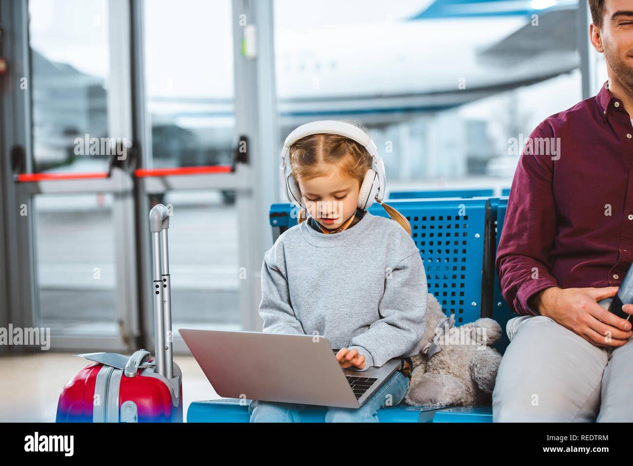 adorable child in headphones using laptop near dad in waiting hall Stock Photo