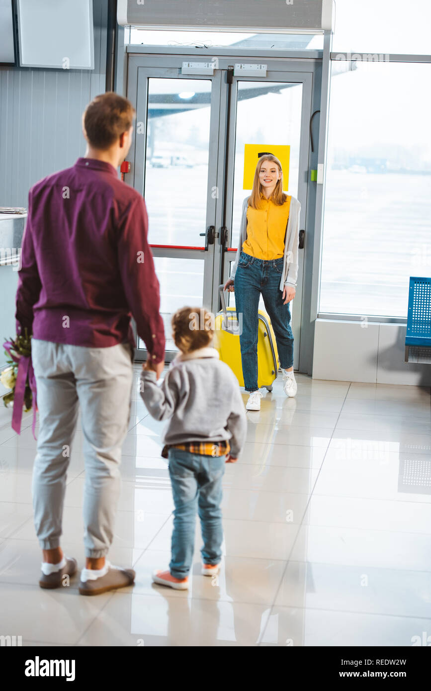 back view of man holding hands with daughter and looking at wife with luggage Stock Photo
