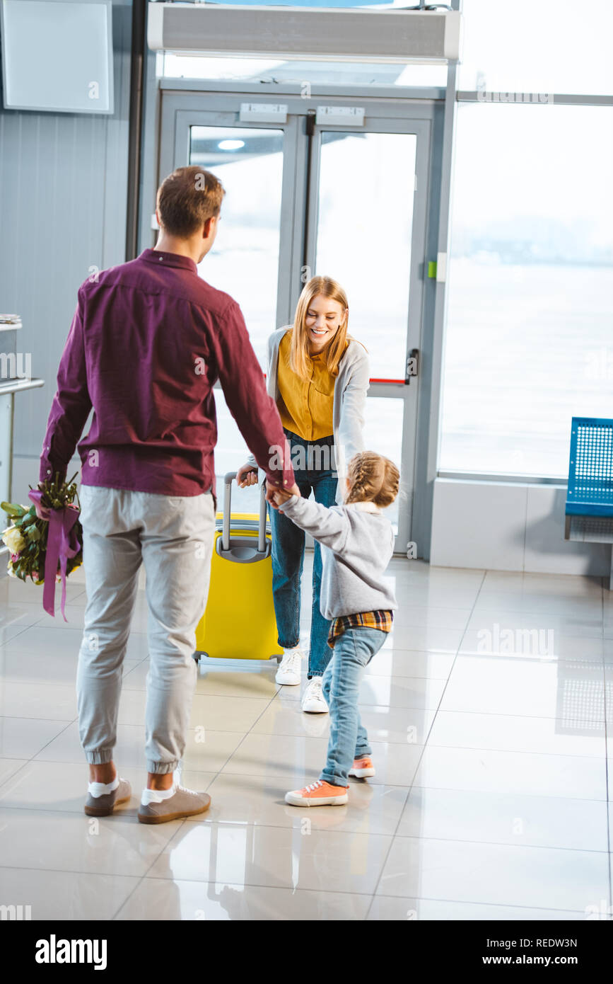mother with baggage looking at husband and daughter holding hands while meeting in airport Stock Photo