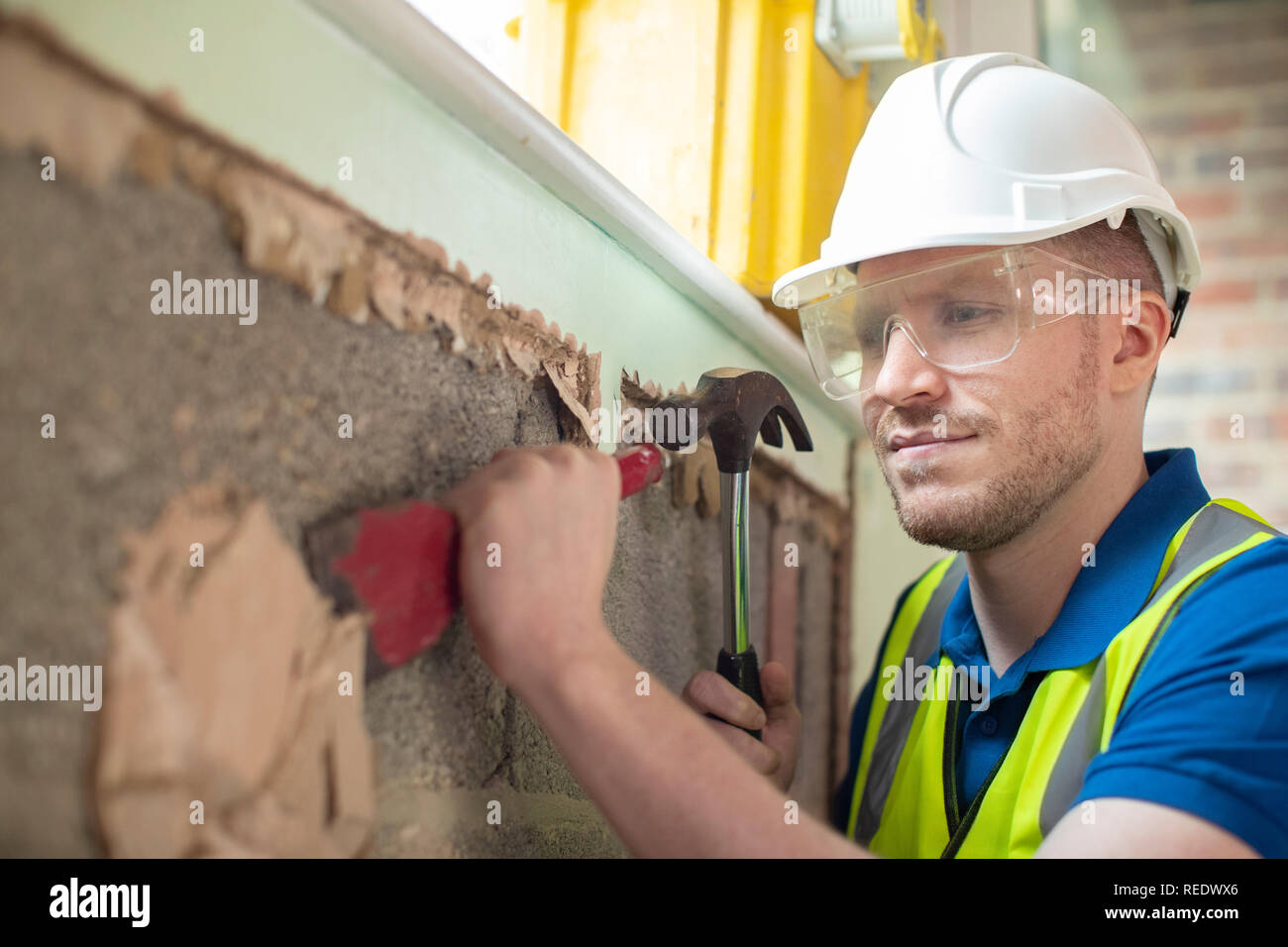 Construction Worker With Chisel Removing Plaster From Wall In Renovated House Stock Photo