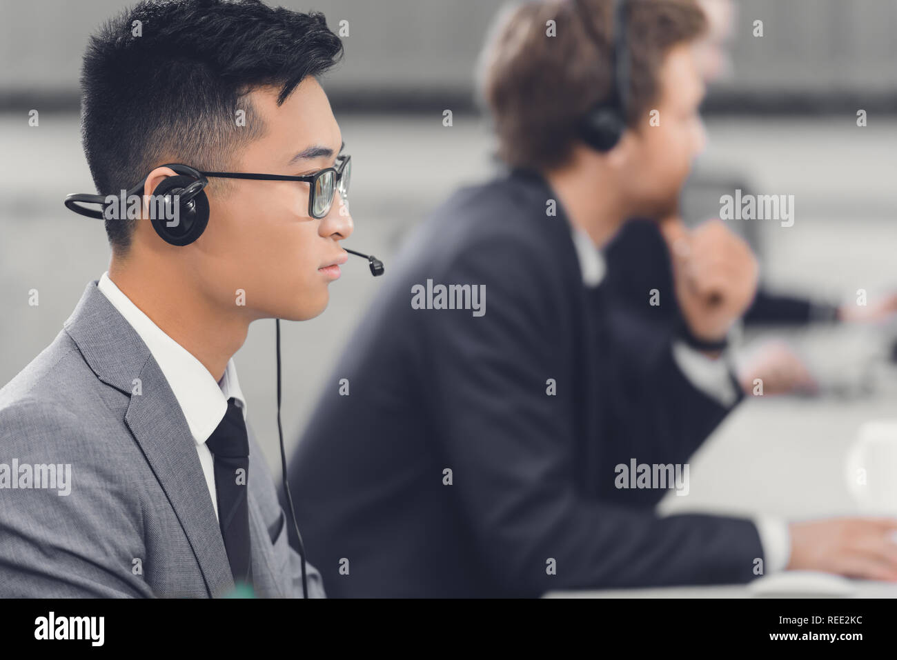 side view of focused young asian businessman in headset working with colleagues in office Stock Photo