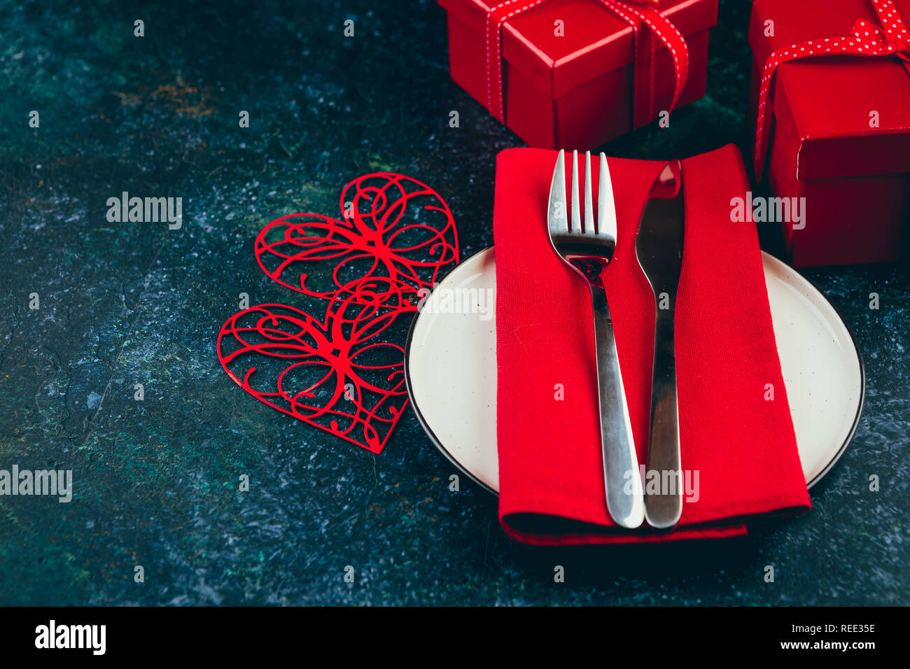 Valentine's day table setting. Table set with plate, hearts, red gift boxws, cjocolate sweets, knife and fork onblue background. Top view and copy spa Stock Photo