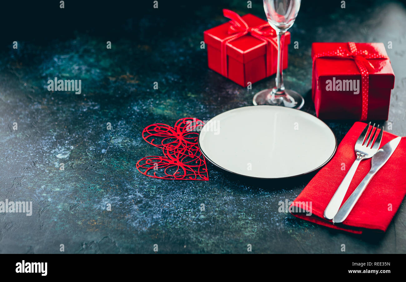 Valentine's day table setting. Table set with plate, hearts, red gift boxws, cjocolate sweets, knife and fork onblue background. Top view and copy spa Stock Photo