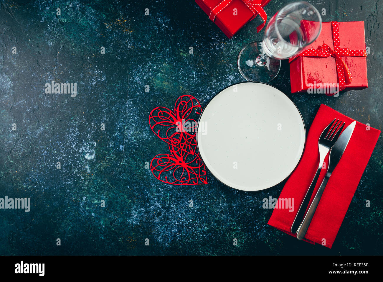 Valentine's day table setting. Table set with plate, hearts, red gift boxws, cjocolate sweets, knife and fork onblue background. Top view and copy spa Stock Photo