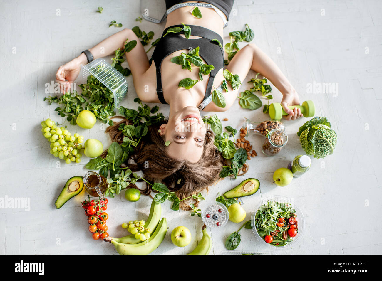 Beauty portrait of a sports woman surrounded by various healthy food lying on the floor. Healthy eating and sports lifestyle concept Stock Photo