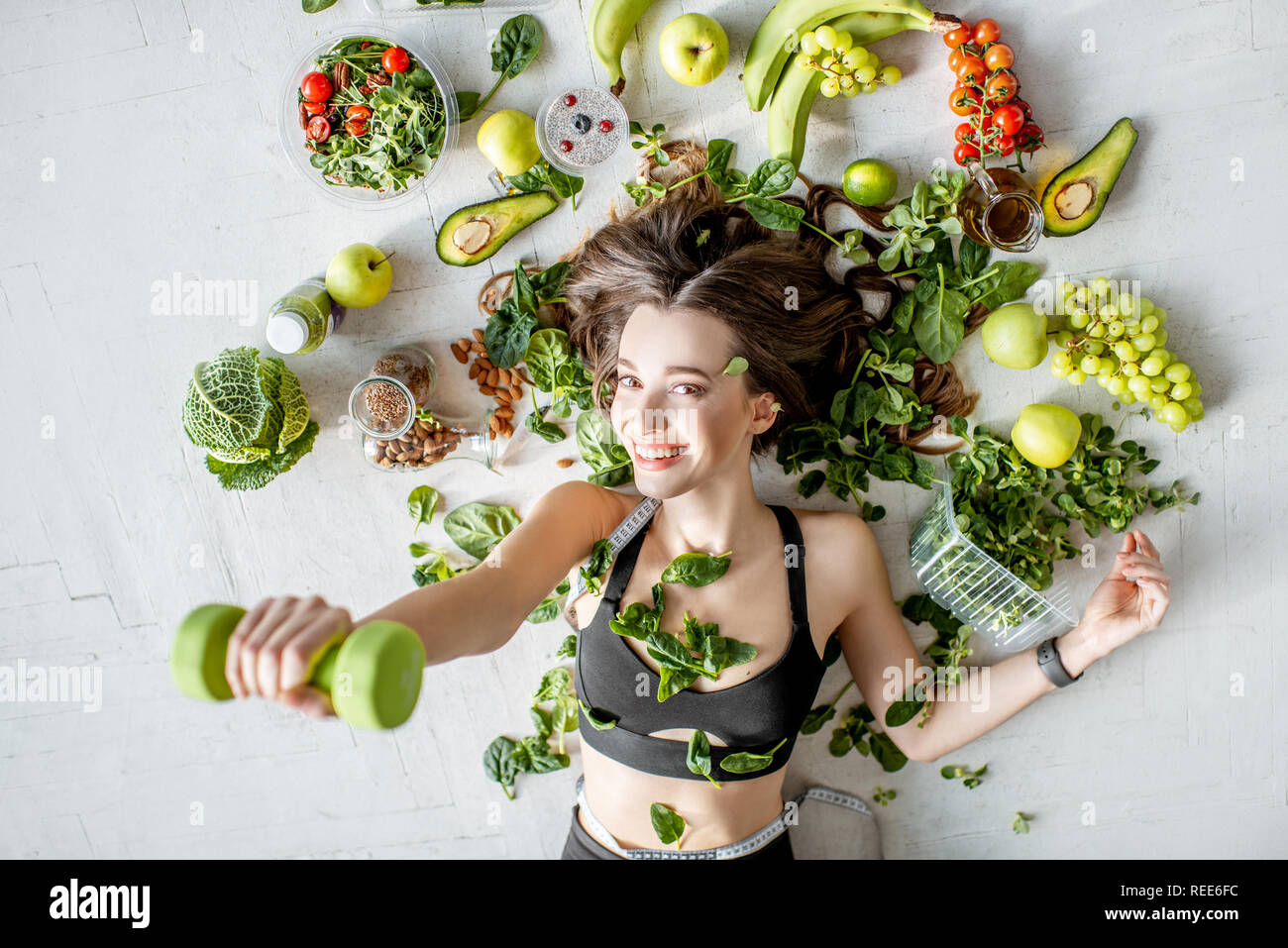 Beauty portrait of a sports woman surrounded by various healthy food lying on the floor. Healthy eating and sports lifestyle concept Stock Photo