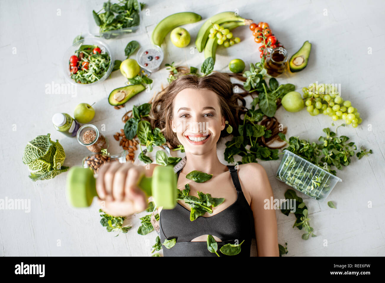 Beauty portrait of a sports woman surrounded by various healthy food lying on the floor. Healthy eating and sports lifestyle concept Stock Photo
