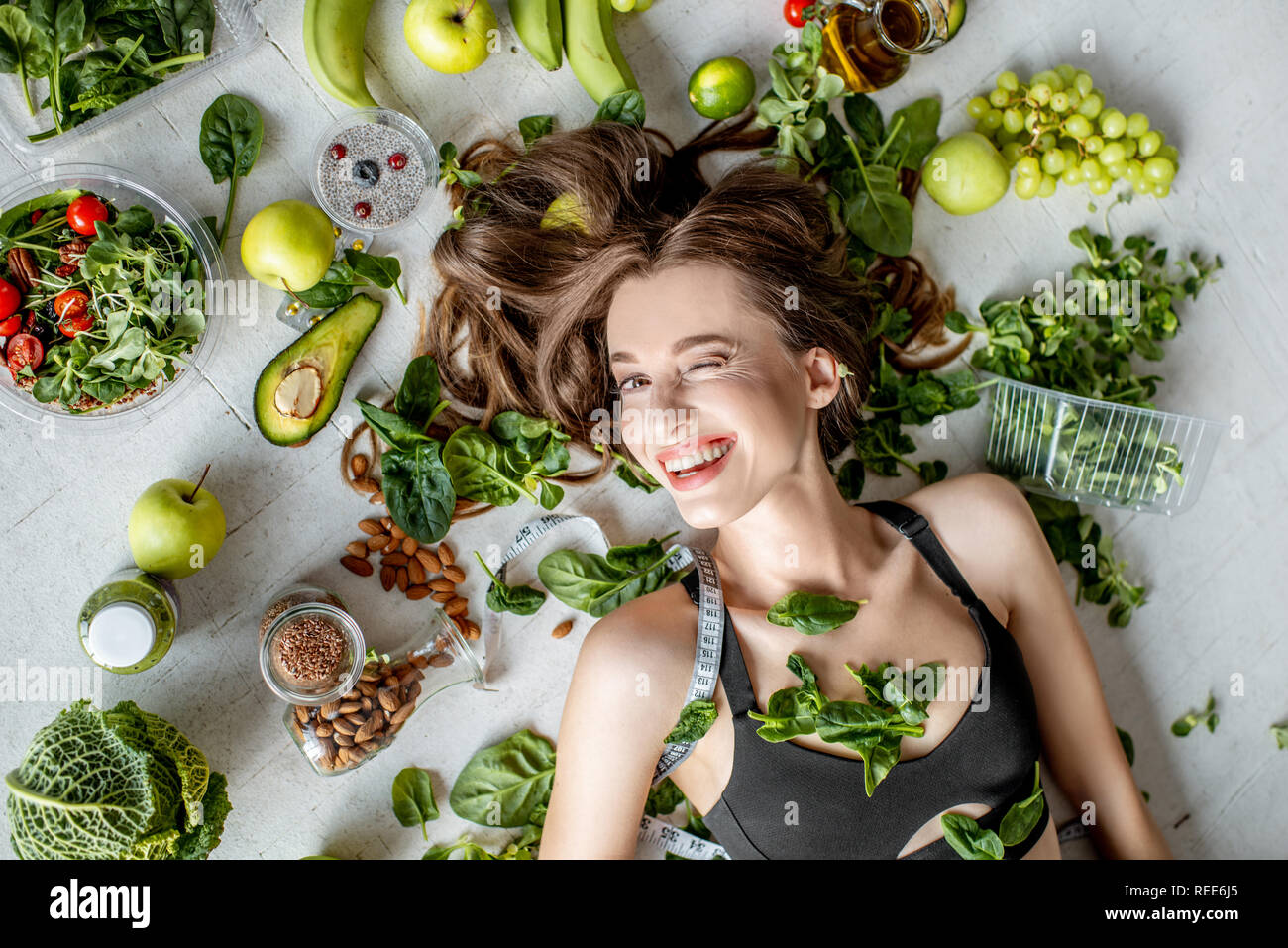 Beauty portrait of a woman surrounded by various healthy food lying on the floor. Healthy eating and sports lifestyle concept Stock Photo