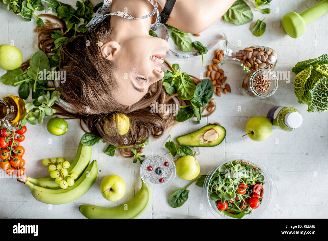 Beauty portrait of a woman surrounded by various healthy food lying on the floor. Healthy eating and sports lifestyle concept Stock Photo