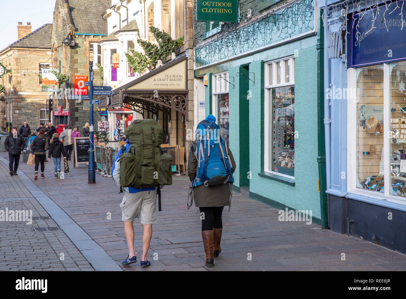 Male and female hikers walking through Keswick town centre carrying walking backpacks,Keswick,Lake District,Cumbria,England Stock Photo