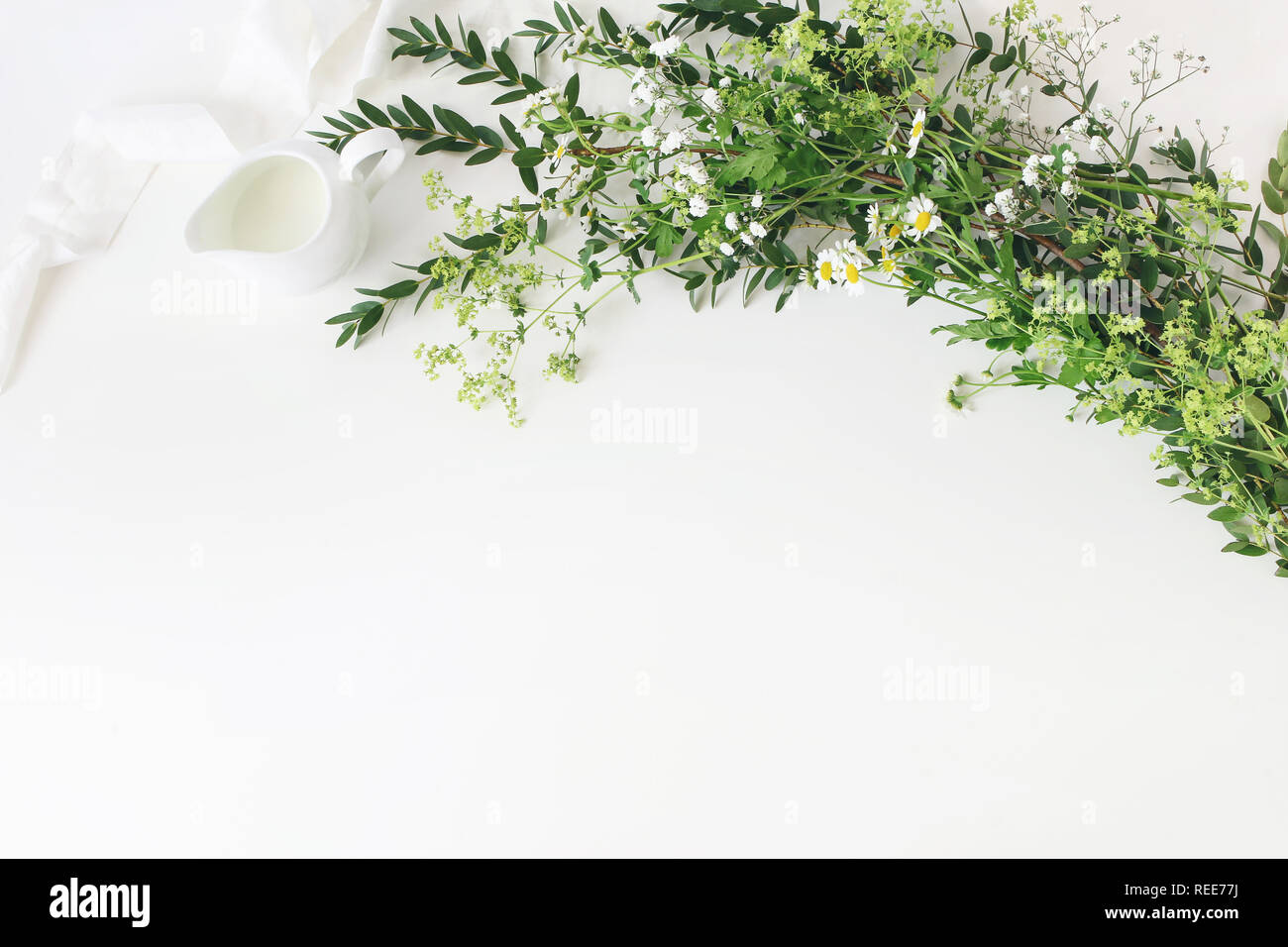 Festive wedding, birthday table scene with eucalyptus parvifolia, silk ribbon, wild meadow flowers and milk pitcher on white table background. Rustic  Stock Photo