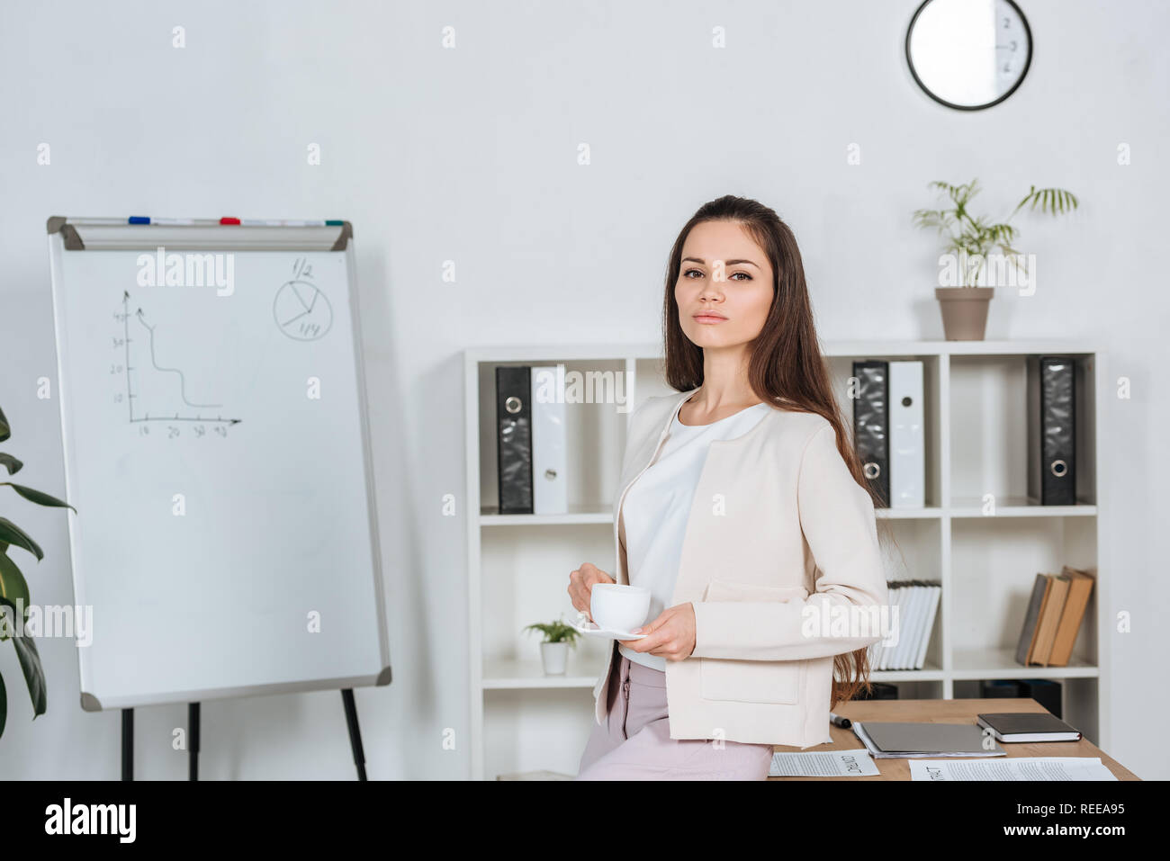 beautiful young businesswoman holding cup of coffee and looking at ...