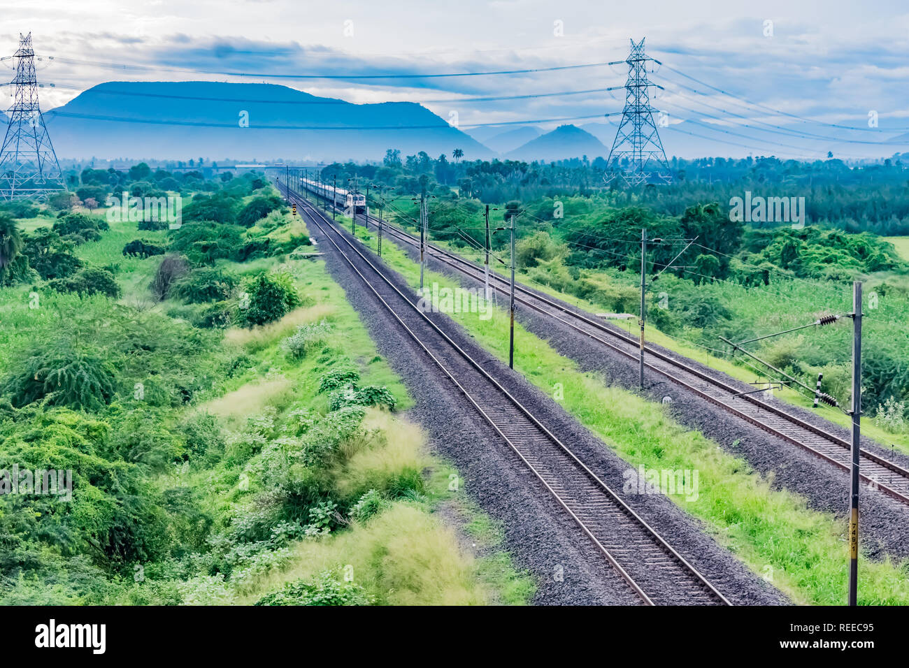 straight railway track goes to the horizon in the green landscape under the blue sky with clouds. Stock Photo