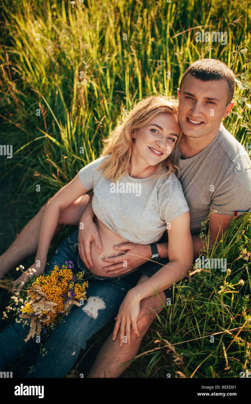 A young man embraces the belly of his pregnant wife while walking ...