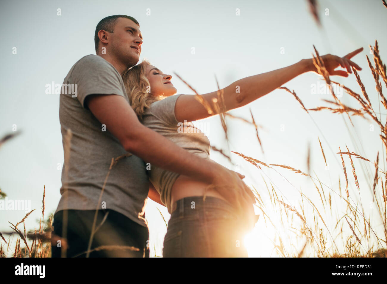 A young man embraces the belly of his pregnant wife during a walk ...
