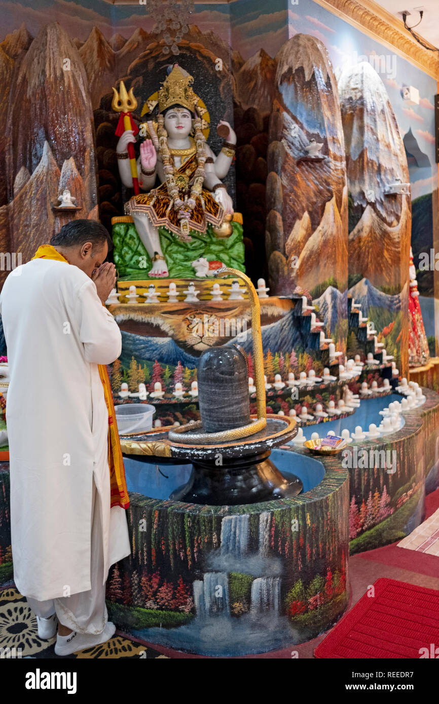 A Hindu priest praying and meditating in front of a lingam and likeness of the goddess Shiva. At a temple in South Richmond Hill, Queens, New York. Stock Photo
