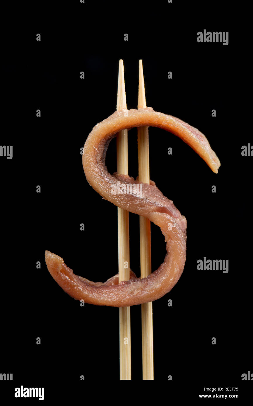 An achovy fillet on two cocktail sticks in the form of a US dollar sign photographed on a black background. England UK GB Stock Photo