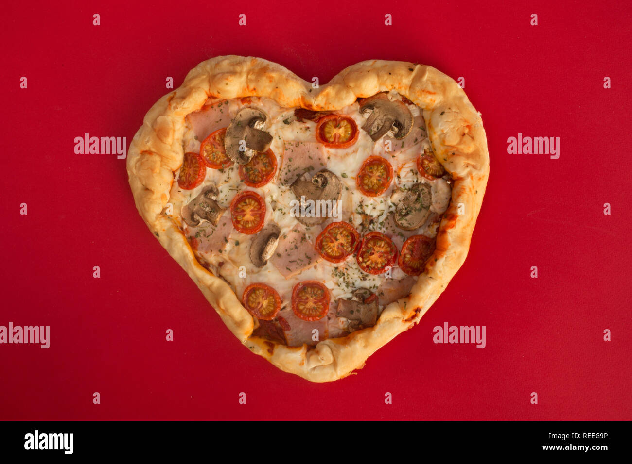 Pizza heart shaped with ham tomatoes and mushrooms on red background .  Concept of romantic love for Valentines Day . Love food Stock Photo - Alamy