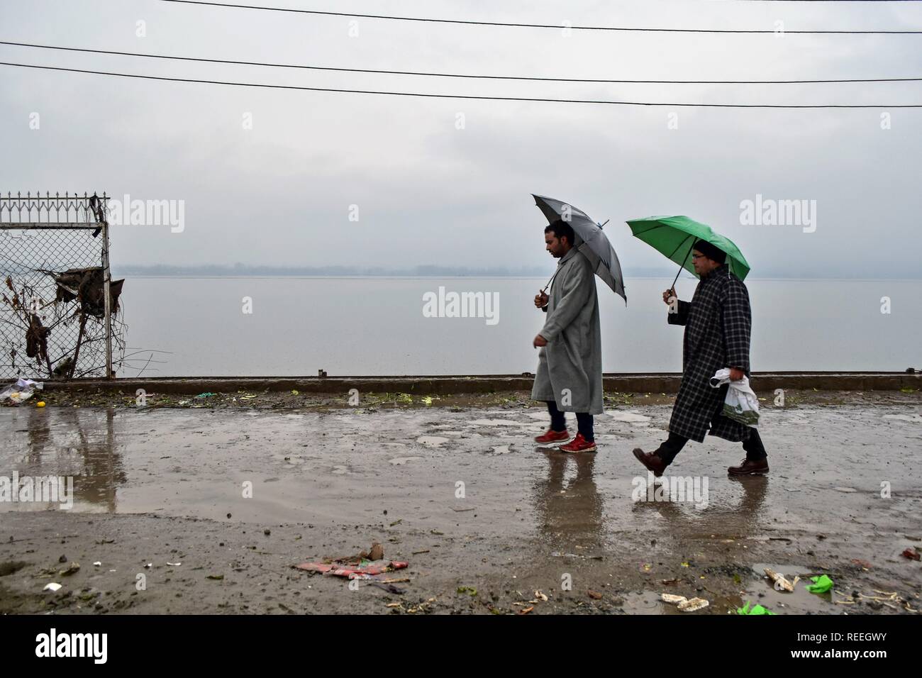 Kashmiri residents hold umbrellas as they walk during rainfall in Srinagar, Indian administered Kashmir. The upper reaches on Monday received fresh snowfall, while rains lashed Srinagar, and other parts of the Kashmir valley. The weather man has forecast moderate to heavy rain and snowfall over the state during the next 24 hours. Stock Photo