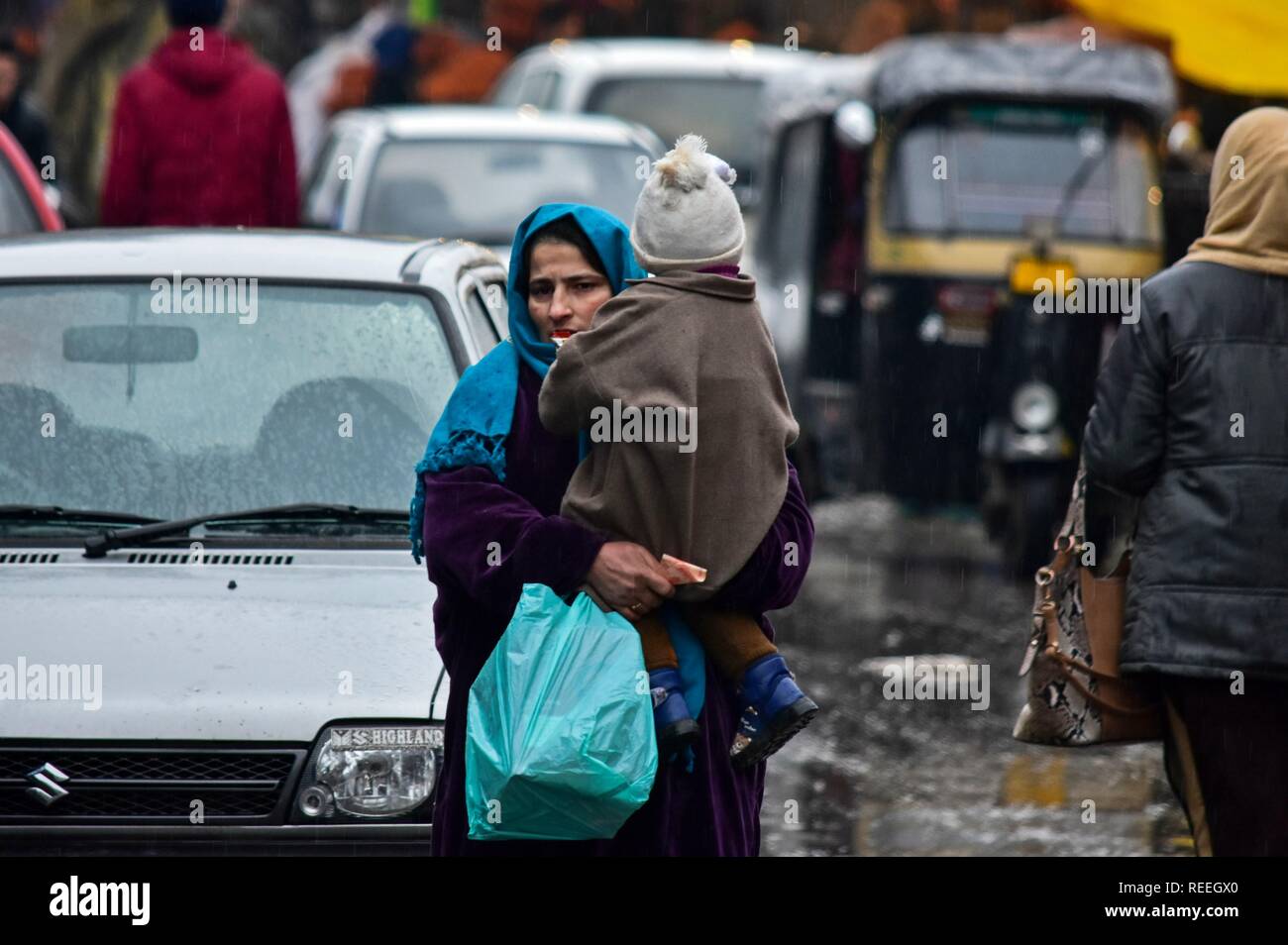 A woman carries her child as she walks through a street during rainfall in Srinagar, Indian administered Kashmir. The upper reaches on Monday received fresh snowfall, while rains lashed Srinagar, and other parts of the Kashmir valley. The weather man has forecast moderate to heavy rain and snowfall over the state during the next 24 hours. Stock Photo