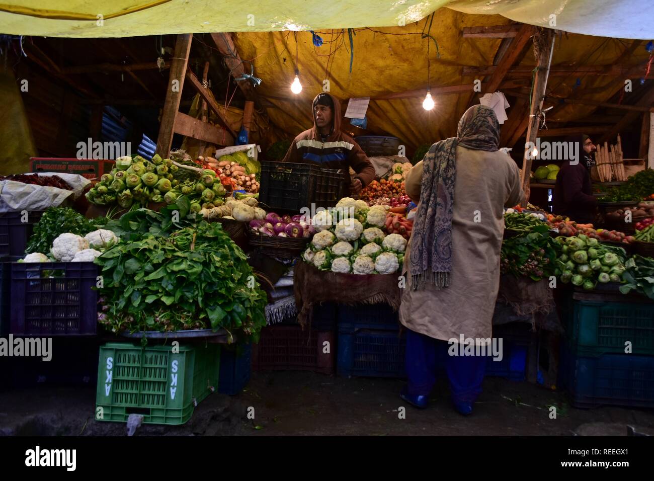A Kashmiri vendor sell vegetables to a customer at a market during rainfall in Srinagar, Indian administered Kashmir. The upper reaches on Monday received fresh snowfall, while rains lashed Srinagar, and other parts of the Kashmir valley. The weather man has forecast moderate to heavy rain and snowfall over the state during the next 24 hours. Stock Photo