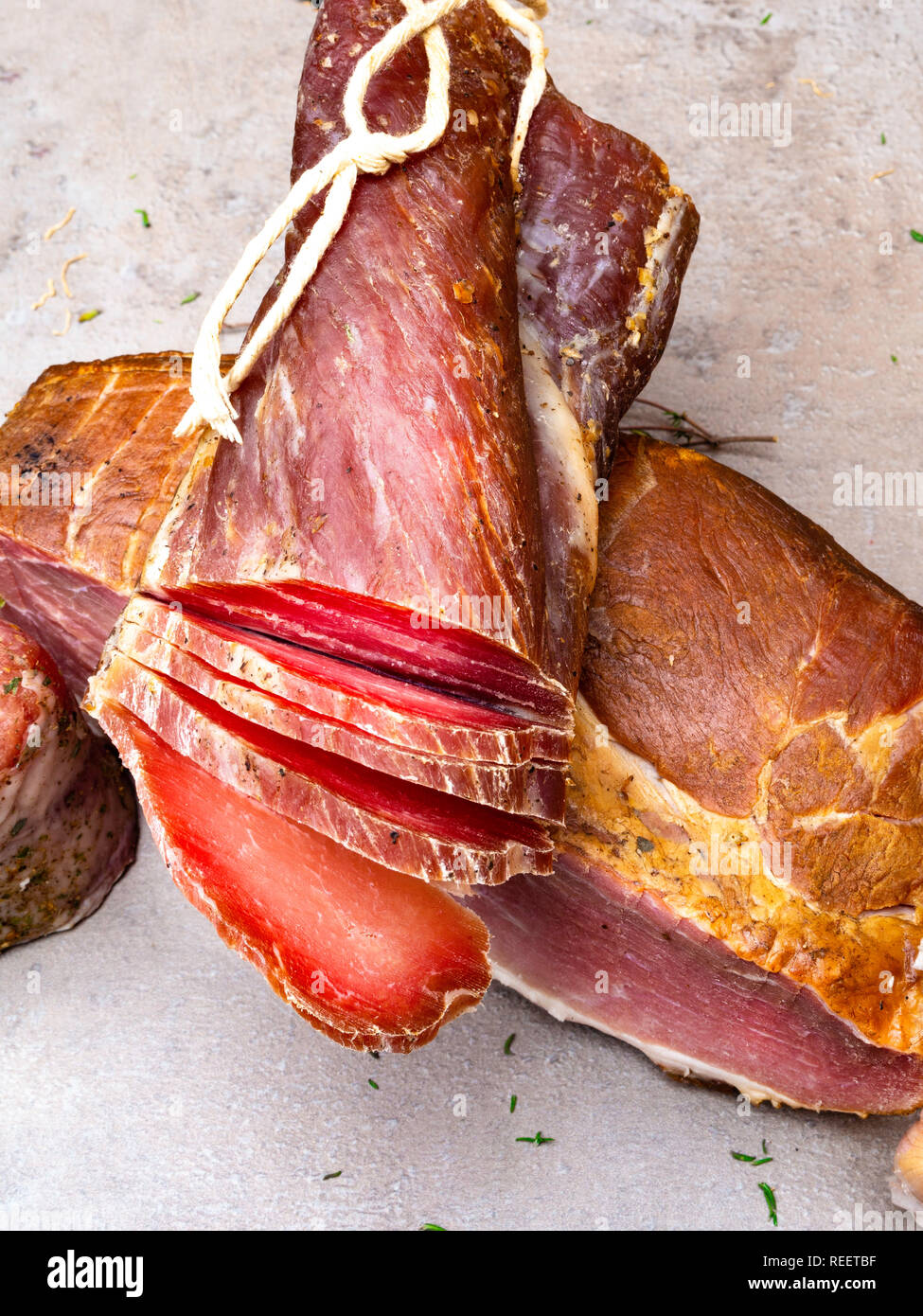 Smoked ham, jerky corned beef on table with garlic, herbs on stone