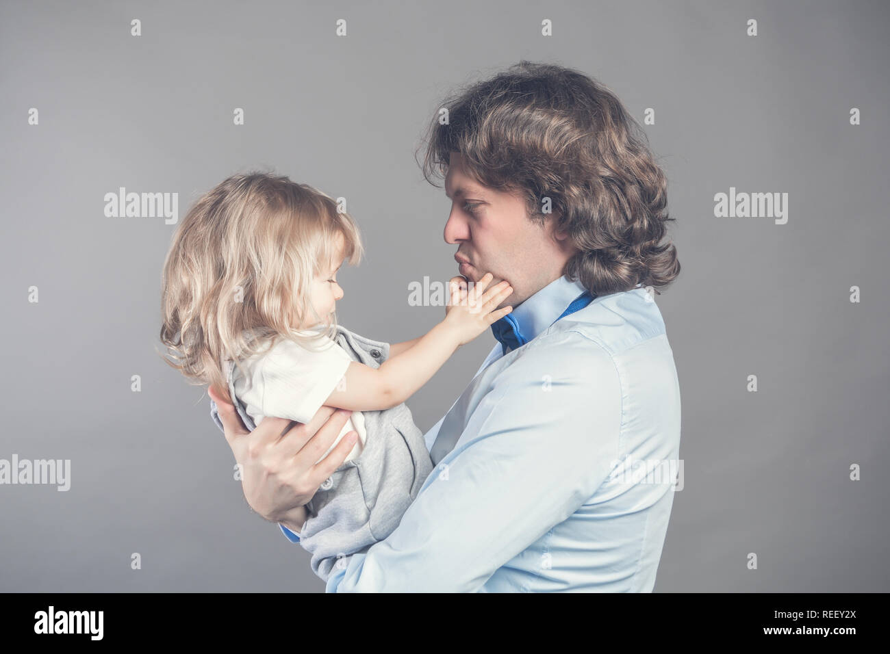 Happy smiling father holding on hands preschool daughter, looking at each other, father standing on grey studio background together with little girl.  Stock Photo