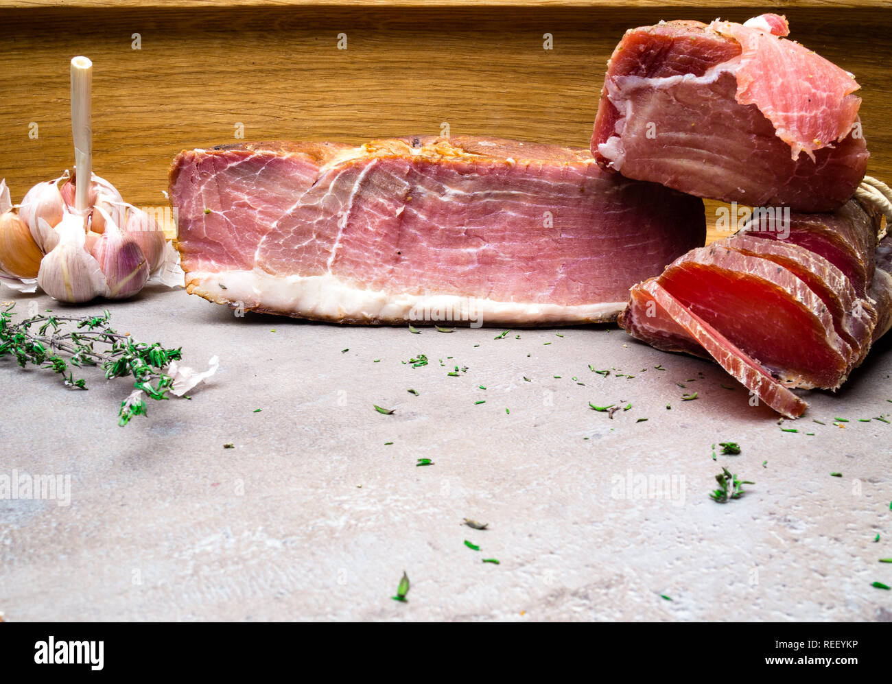 Homemade glazed smoked ham, salted meat, jerky with fresh natural herbs and aromatic spices on stone table copy space Stock Photo