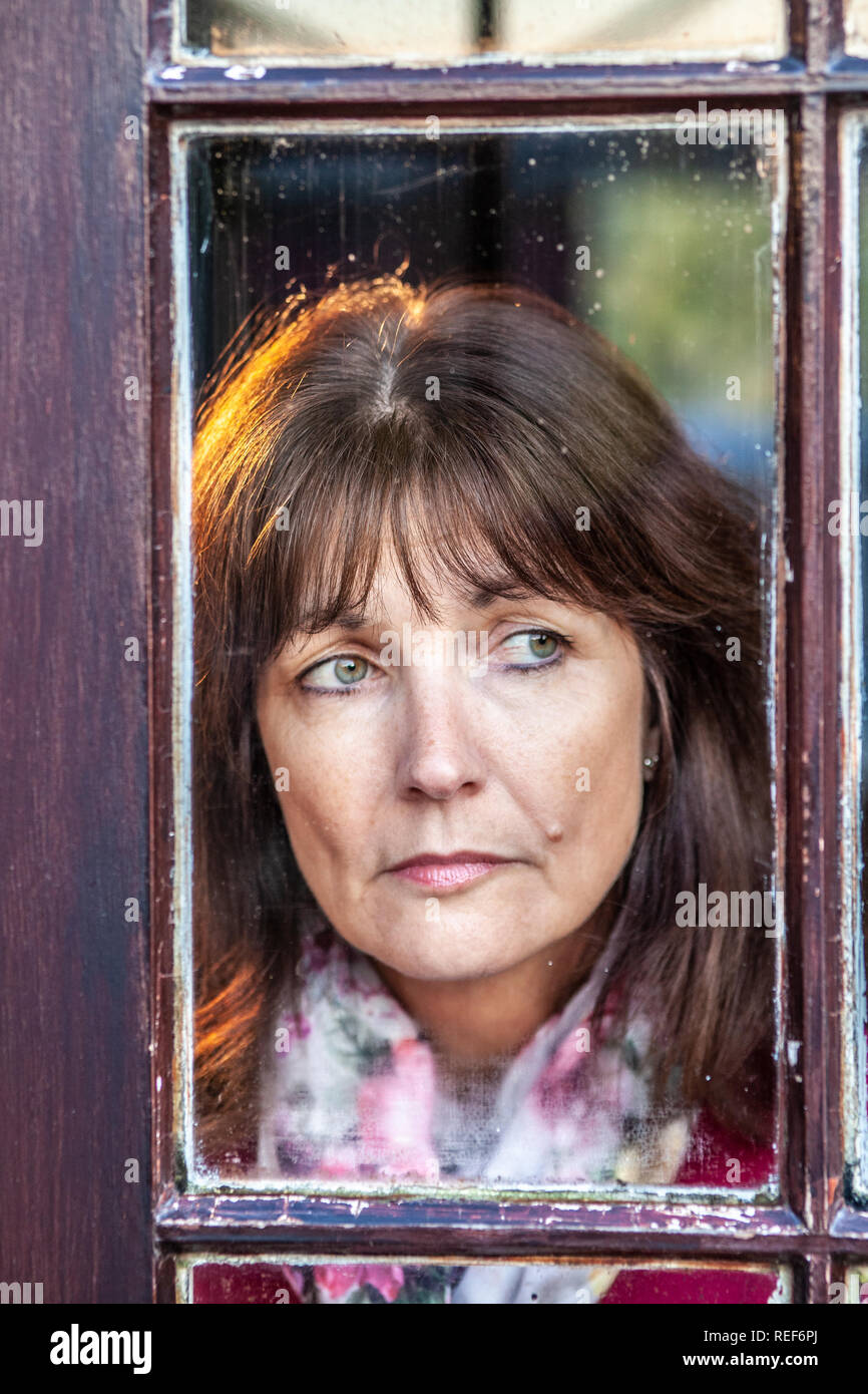 Model released attractive, single woman, looking out of a window Stock Photo