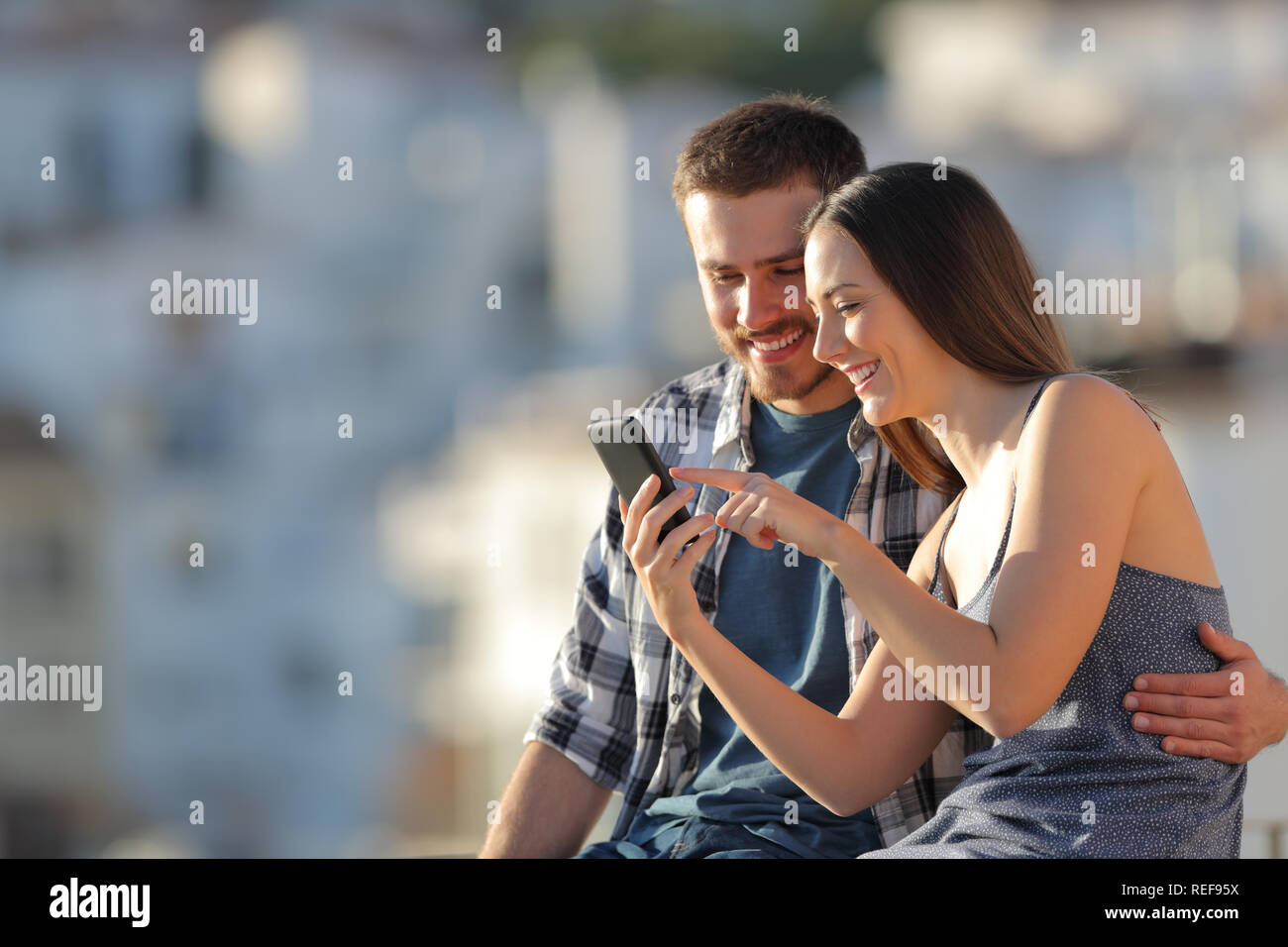 Happy couple browsing smart phone content in a town outskirts at sunset Stock Photo