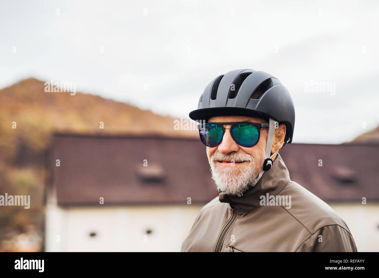Active senior man with bike helmet and sunglasses standing outdoors in