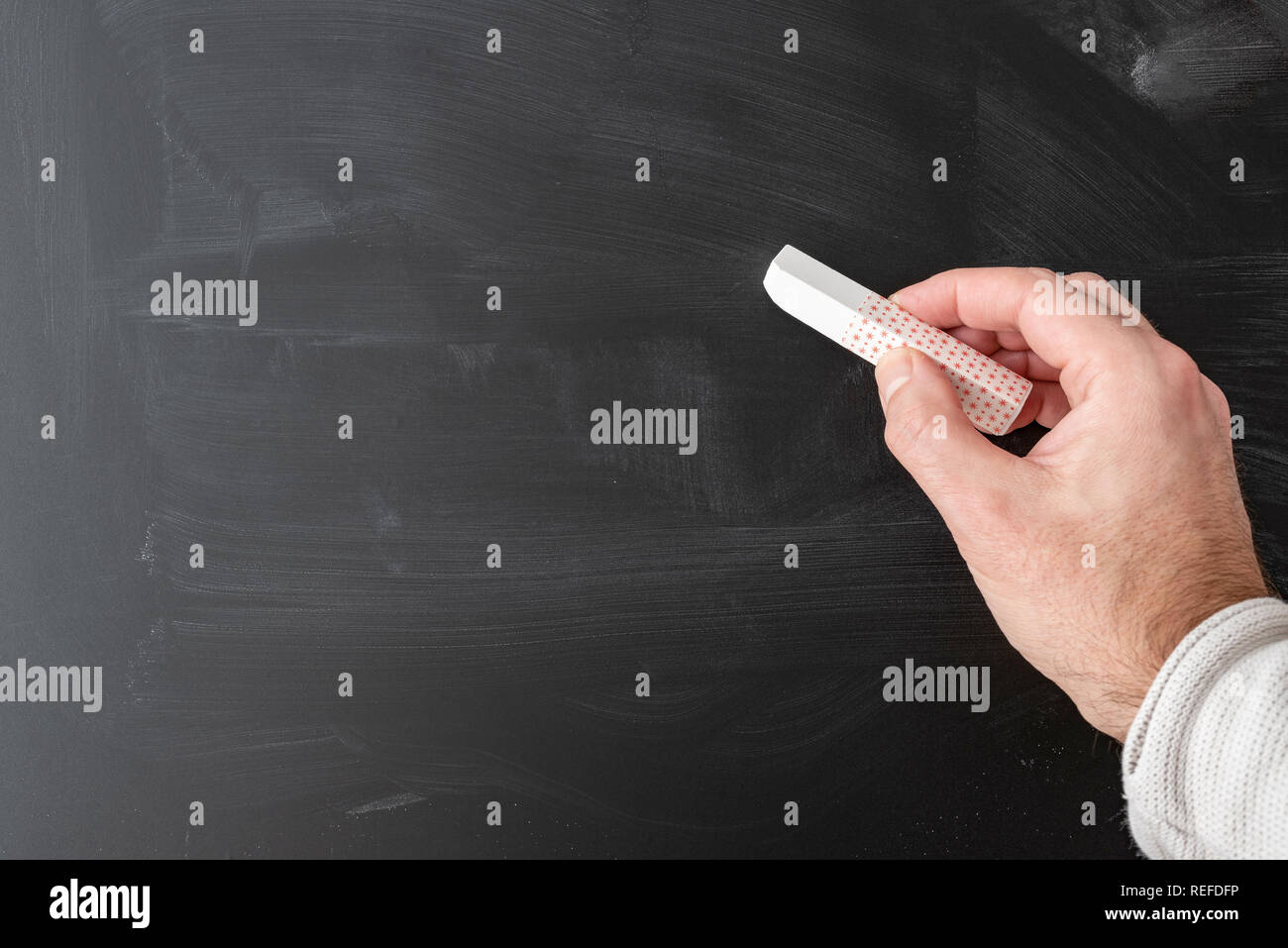hand holding stick of chalk against chalkboard  Stock Photo