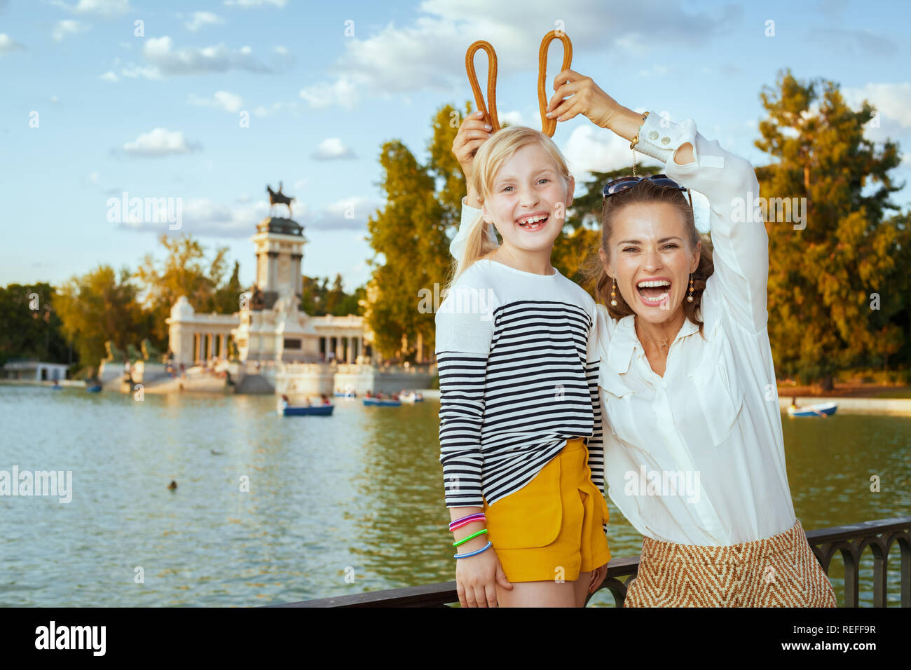 smiling trendy mother and daughter tourists making horns with traditional Spain churro at Park del Retiro. churros - classic Madrid sweet snack. famil Stock Photo