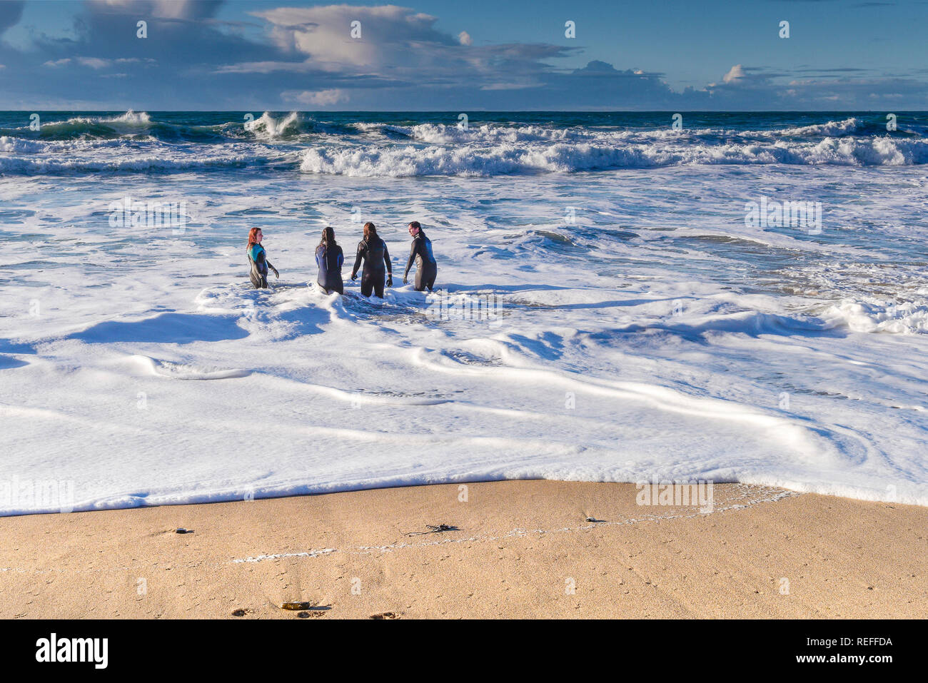 People in wetsuits standing in the sea at Fistral Beach in Newquay Cornwall. Stock Photo