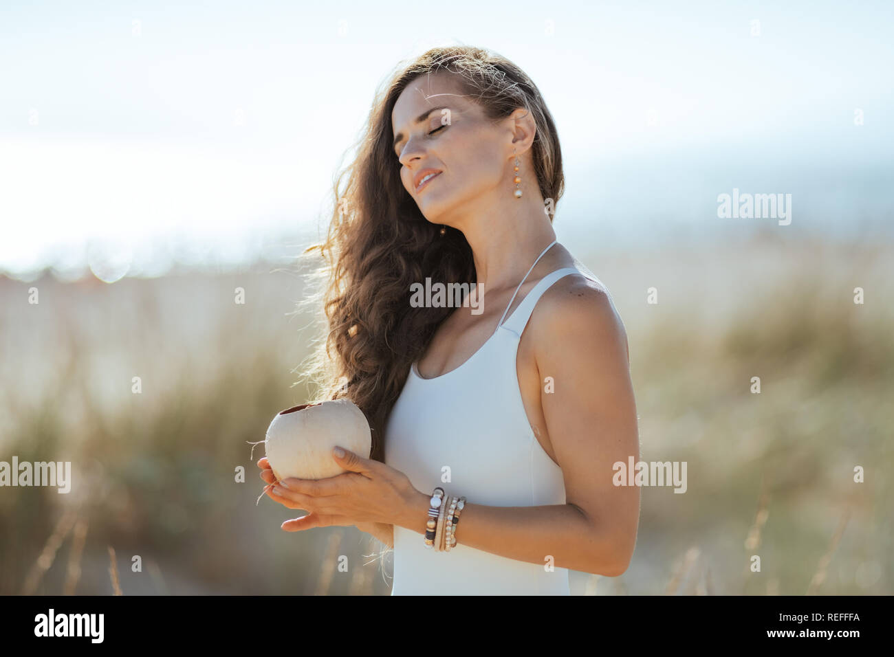 Relaxed Modern Woman In White Beachwear On The Ocean Coast Holding