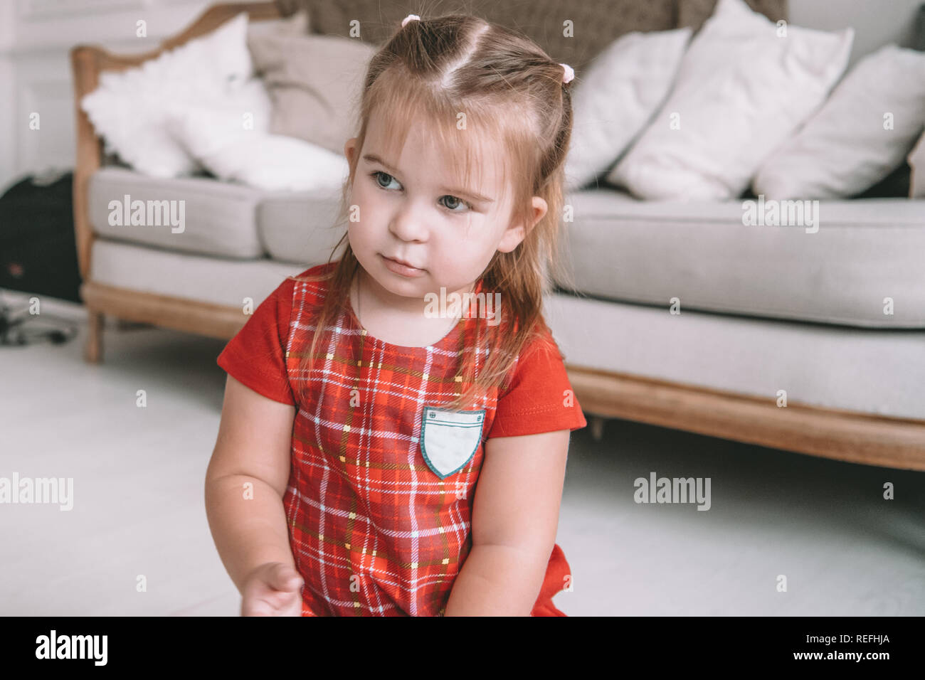 Close up little adorable thoughtful girl dreaming sitting on a floor in a living room at modern home Stock Photo