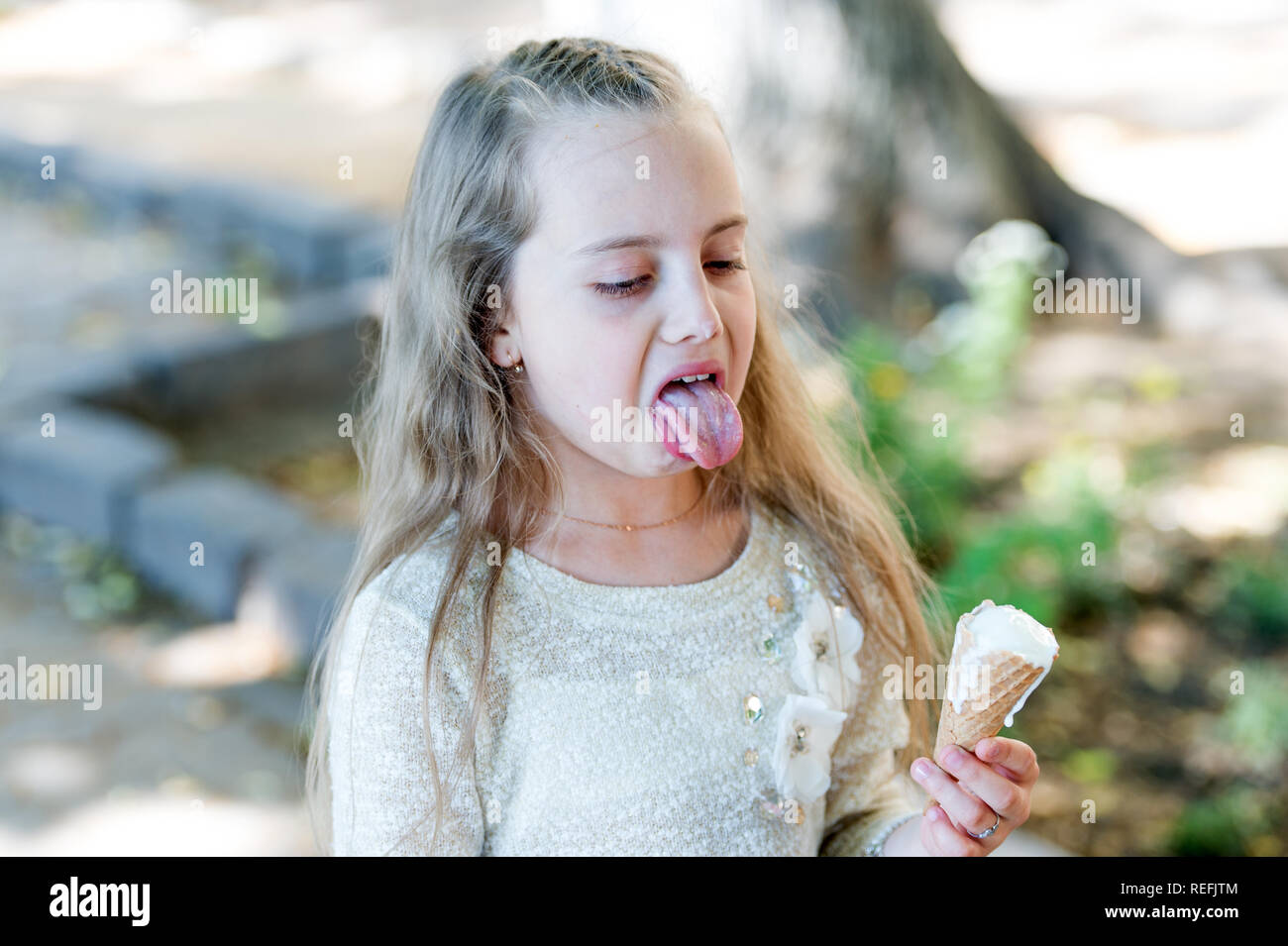 Kid girl with ice cream cone in hand. Summer treats concept. Sweet tooth girl child with white ice cream in waffle cone. Girl sweet tooth on disgusted face eats ice cream, light background. Stock Photo
