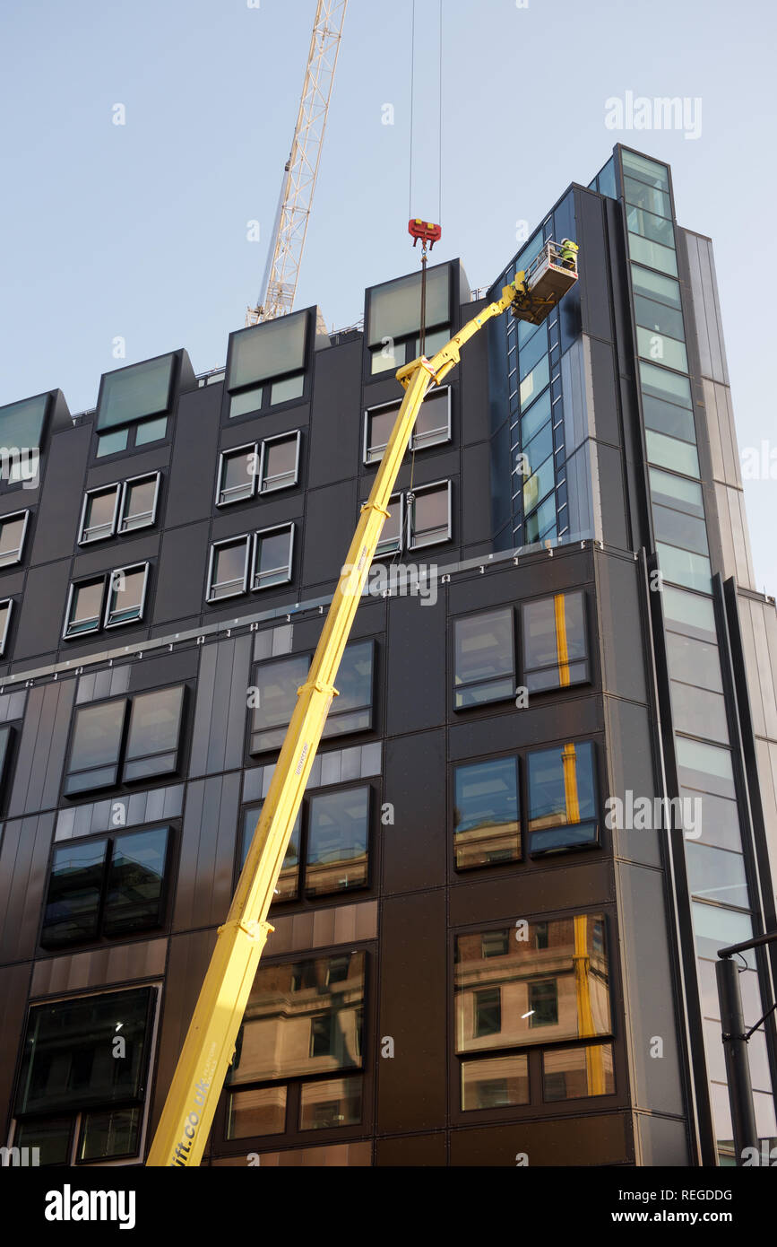 Workman operating machinery at the top of a tall building Stock Photo
