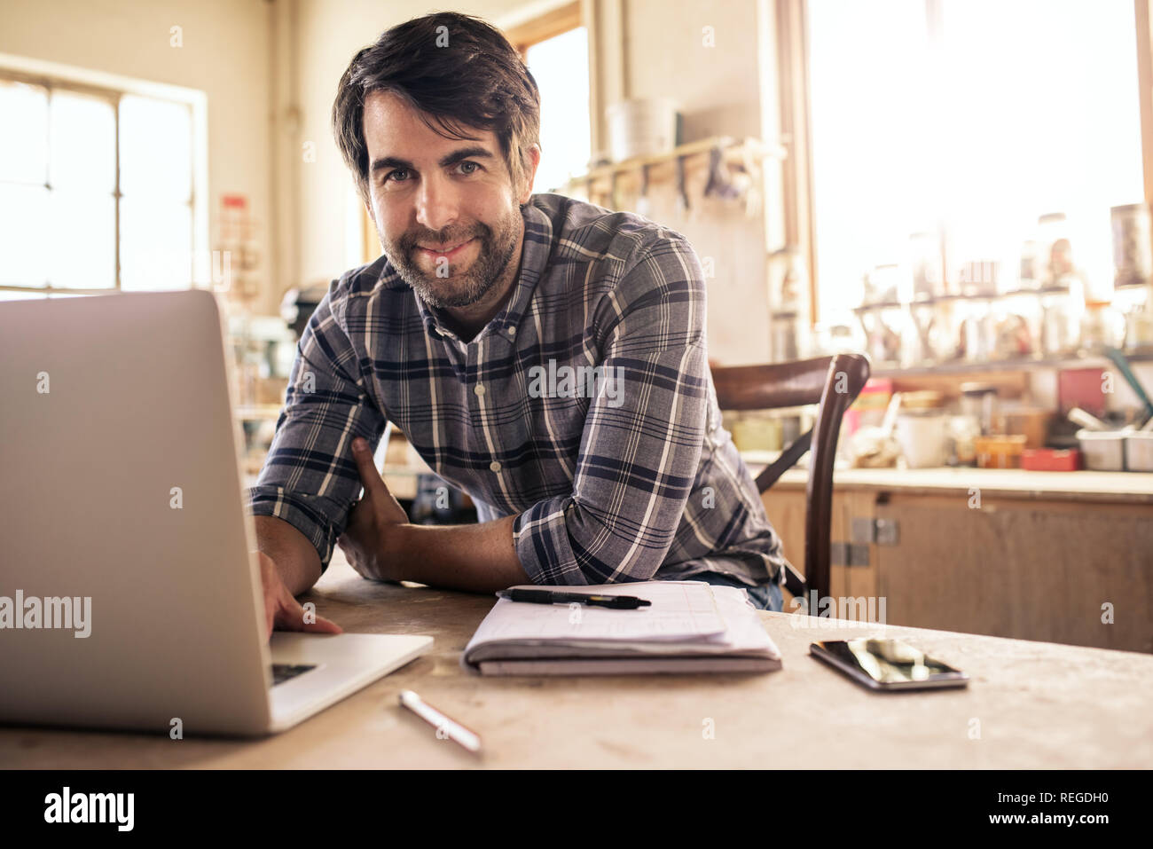 Smiling woodworker using a laptop in his workshop Stock Photo