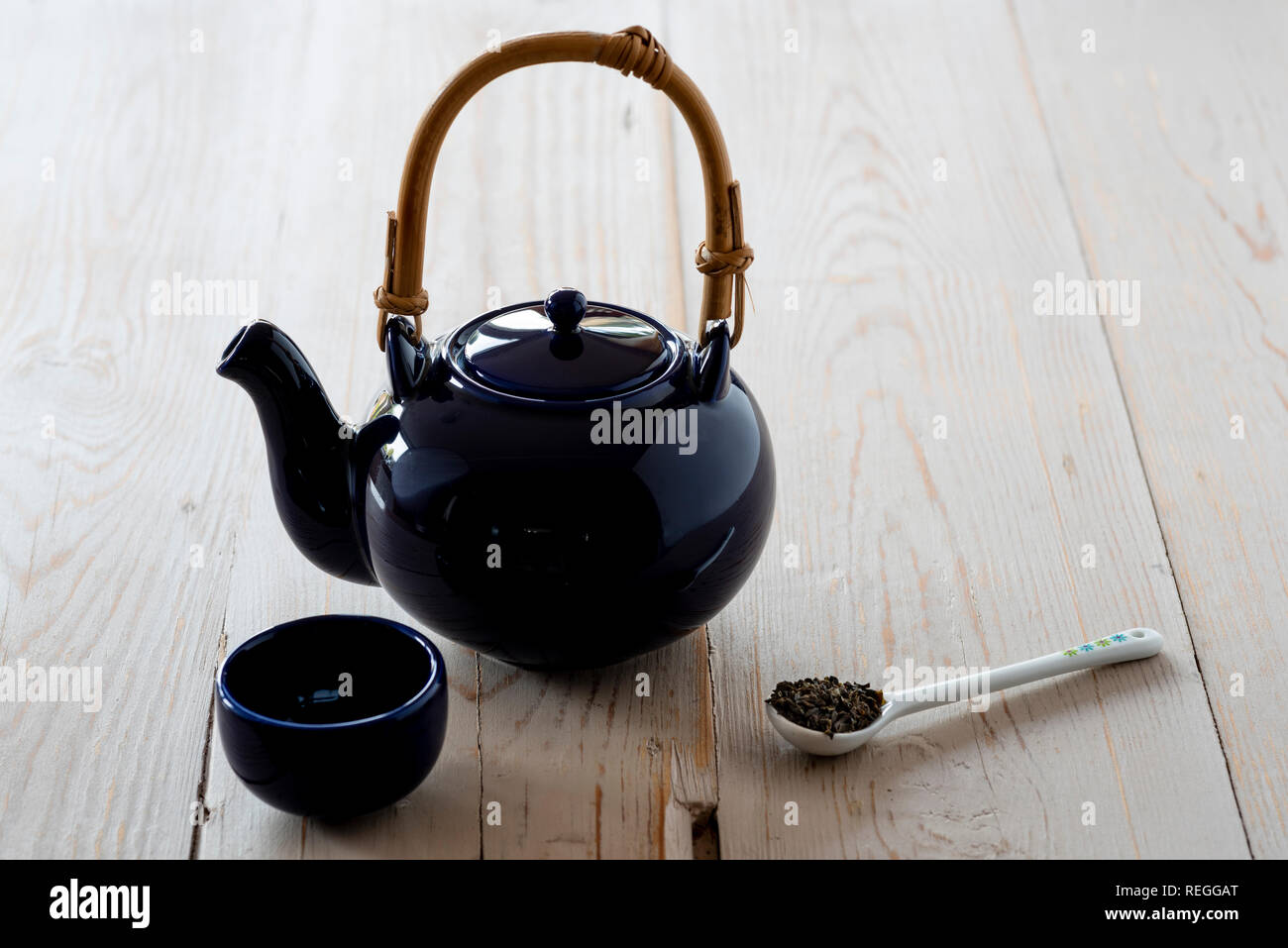 View of oriental teapot and cup, with green tea leaves. Stock Photo