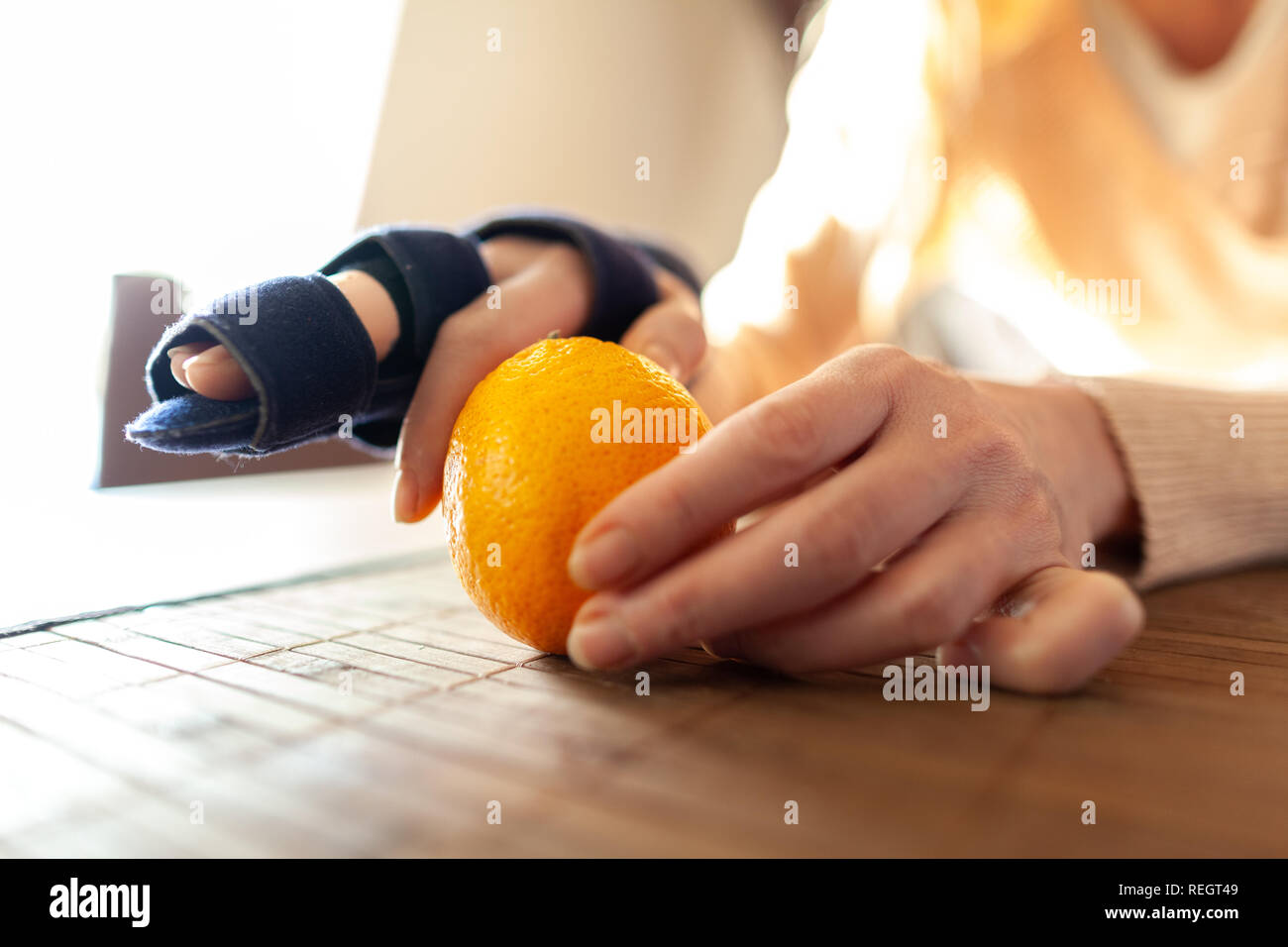 A hand peels an orange with a medical hand sling Stock Photo