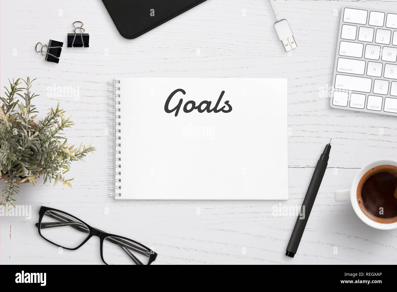 Creating goals list on notepad on office desk surrounded with office supplies. White wooden work desk. Stock Photo