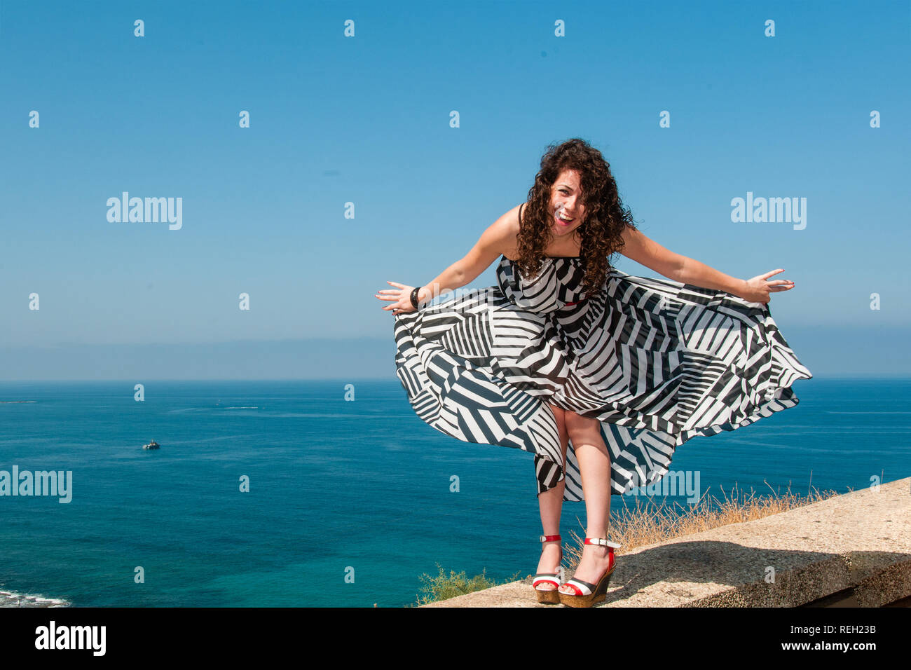 Portrait of a laughing girl in a light dress against the blue sea on a warm summer day Stock Photo