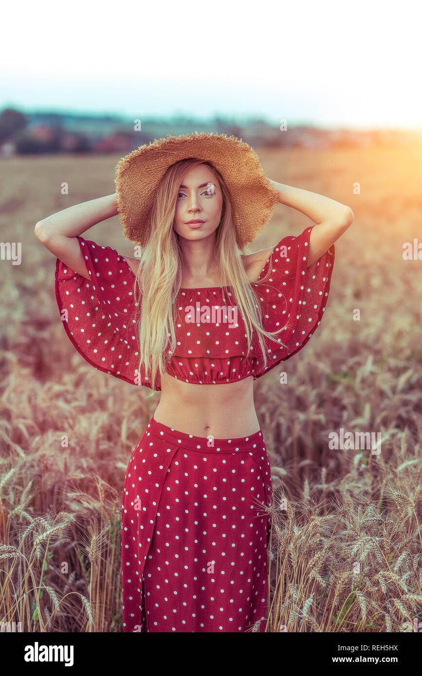 A beautiful girl in red dress is standing in a wheat field and ...
