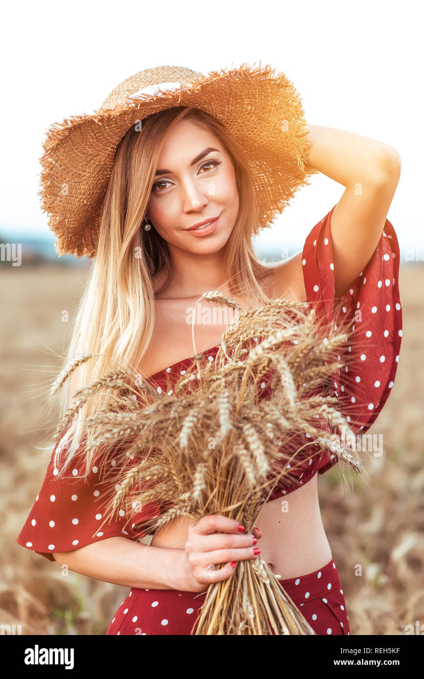 Beautiful girl in a red dress standing in a wheat field and a straw hat ...