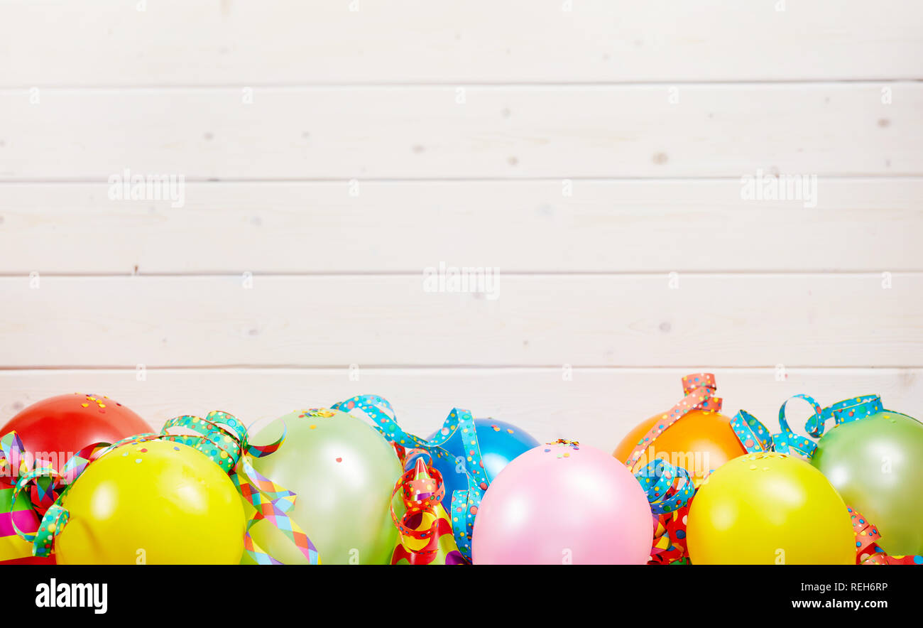 Colorful party background with copy space over white wooden boards and a border of colorful balloons and streamers Stock Photo