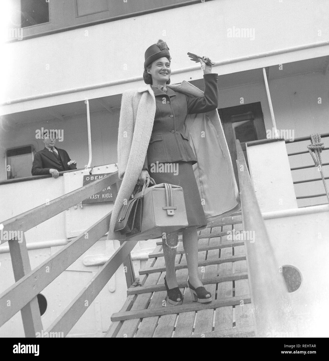 Women's fashion in the 1940s. A young woman in a typical 1940s jacket and skirt, with matching hat, shoes, gloves and handbag. She waves at someone waiting for her on the quay when arriving after travelling with a passenger ship.  Photo Kristoffersson Ref V77-1. Sweden 1947 Stock Photo
