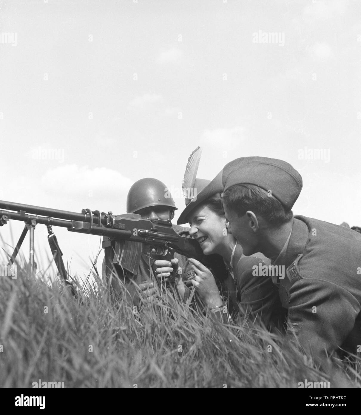 The Regiment's day in the 1940s. A fashionable looking lady is behind a machinegun together with two soldiers. She aims carefully, closing one eye. Sweden 1942 Photo Kristoffersson C20-3 Stock Photo