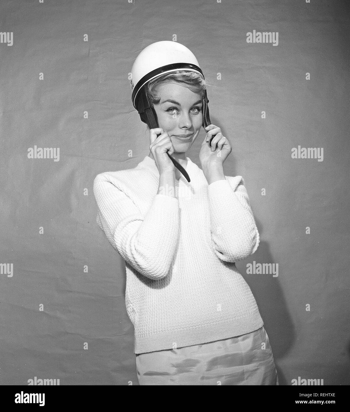 Woman in the 1950s. A young woman is standing dressed in a typical 50s sweater. She is putting on a white moped helmet.  Photo Kristoffersson ref BZ8-6. Sweden 1952 Stock Photo